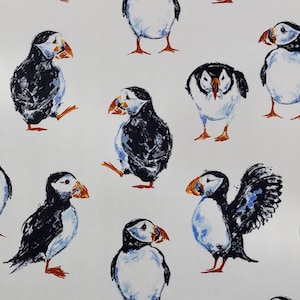 May include: A repeating pattern featuring puffin birds on a white backdrop. The birds are illustrated in a watercolour style, with black, white, and blue plumage, and orange beaks and feet. The puffins are shown in different poses.