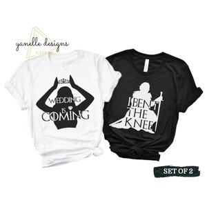 May include: Set of two white t-shirts with black text and graphics. The first shirt features a silhouette of a woman with a crown above her head and the text "Wedding is Coming". The second shirt features a silhouette of a man with a sword and the text "I Bent the Knee".