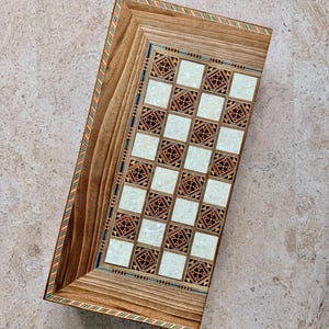 May include: A rectangular wooden tray featuring a central grid of alternating white mother-of-pearl squares and intricate geometric marquetry squares. The tray is framed by natural wood grain borders with thin, colorful striped inlay accents.