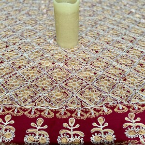 May include: A red tablecloth with a white and gold embroidered pattern. The pattern features a repeating design of small flowers and geometric shapes.