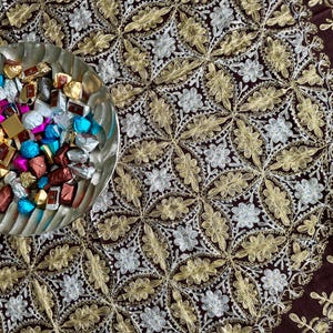 Könnte beinhalten: Eine silberne Schale gefüllt mit verschiedenen Schokoladen, die in bunten Folien verpackt sind. Die Schale steht auf einer braunen Tischdecke mit einem goldenen und silbernen Blumendesign.
