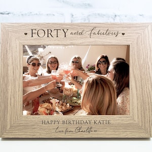 Op de afbeelding: Een licht houten fotolijst met een gepersonaliseerd bericht dat "FORTY and fabulous" en "HAPPY BIRTHDAY KATIE Love from Charlotte xx" luidt. De lijst bevat een foto van een groep vrienden die met drankjes vieren.