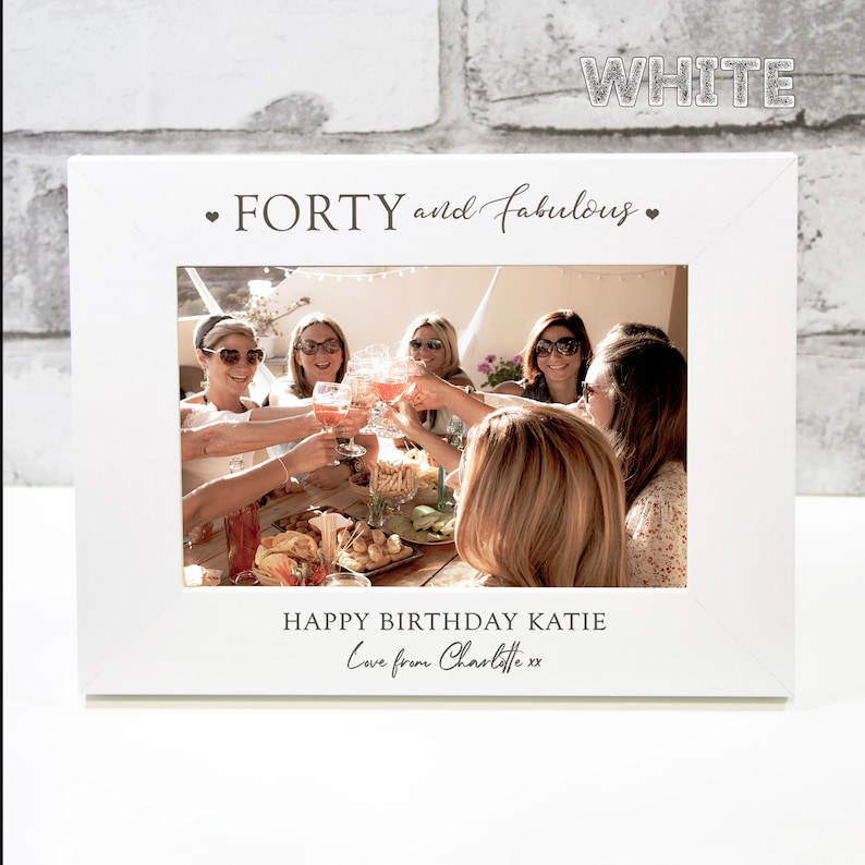 Op de afbeelding: Wit fotolijstje met de tekst "FORTY and fabulous" en een foto van een groep vrienden die feest vieren. De tekst "HAPPY BIRTHDAY KATIE Love from Charlotte xx" is ook inbegrepen.