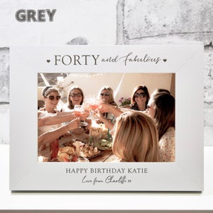 Op de afbeelding: Wit fotolijstje met een zwarte inscriptie die "Forty and Fabulous" en "Happy Birthday Katie Love from Charlotte xx" luidt. Het lijstje bevat een foto van een groep vrouwen die proosten met drankjes.