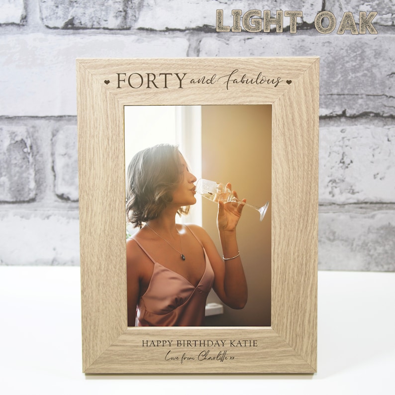 Op de afbeelding: Een fotolijst van licht eikenhout met een gepersonaliseerd bericht dat "FORTY and fabulous" en "HAPPY BIRTHDAY KATIE Love from Charlotte xx" luidt. De lijst bevat een foto van een persoon die een glas champagne vasthoudt.