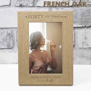 Op de afbeelding: Een houten fotolijst met een lichtbruine afwerking. De lijst heeft een witte passe-partout en een heldere glazen voorkant. De lijst is gegraveerd met de tekst "FORTY and fabulous" en "HAPPY BIRTHDAY KATIE Love from Charlotte xx".