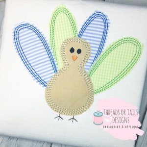 Puede incluir: Diseño de aplique bordado de un pavo marrón con plumas de cuadros azules y verdes. El diseño incluye el texto "Threads or Tails Designs Embroidery & Applique".