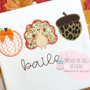 Puede incluir: Una aplicación de tela blanca con un diseño de calabaza, pavo y bellota. La calabaza es naranja con lunares blancos y un tallo marrón. El pavo es marrón con un patrón floral rojo, blanco y verde. La bellota es marrón con un patrón de leopardo. El texto "bailee" está bordado en hilo marrón debajo de la aplicación. El texto "Threads or Tails Designs Embroidery & Applique" está bordado en hilo marrón debajo del texto "bailee".
