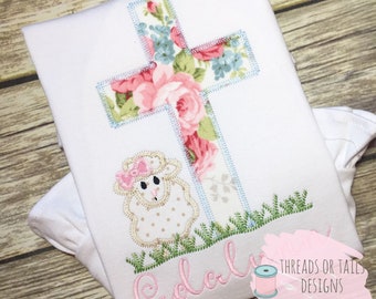 Peut inclure: Chemise blanche brodée avec une croix florale, un agneau et le nom "Eudora" en fil rose. La chemise est réalisée par Threads or Tails Designs, Broderie & Applique.