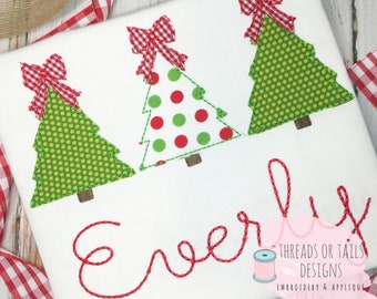 May include: A white t-shirt with three green Christmas trees with red bows and the word "Everly" embroidered in red thread. The text "Threads or Tails Designs Embroidery & Applique" is also embroidered in red thread.