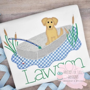 Puede incluir: Dise&ntilde;o bordado de un perro amarillo en un bote de cuadros azules y blancos con una ca&ntilde;a de pescar y un flotador rojo. El dise&ntilde;o est&aacute; en una camiseta blanca con el nombre "Lawson" bordado debajo. El texto "Threads or Tails Designs Embroidery & Applique" tambi&eacute;n est&aacute; bordado en la camiseta.