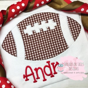 May include: White fabric with a brown and white gingham football applique and the name "Andre" embroidered in red.