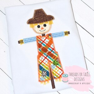 May include: A colorful patchwork scarecrow with a brown hat, blue and white checkered shirt, and orange overalls. The scarecrow is standing on a brown stick with yellow straw hair.