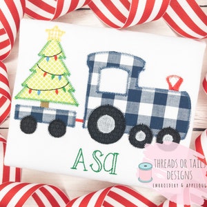 May include: A blue and white checkered train pulls a flatbed wagon carrying a green Christmas tree with yellow lights. The train has a red bell on top. The words "Asa" are embroidered below the train. The words "Threads or Tails Designs Embroidery & Applique" are embroidered in the bottom right corner.