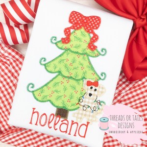 May include: A green Christmas tree with a red bow and a brown bear holding a string of lights. The tree is surrounded by red and white gingham fabric. The text "holland" is embroidered below the tree. The text "Threads or Tails Designs Embroidery & Applique" is in the bottom right corner of the image.