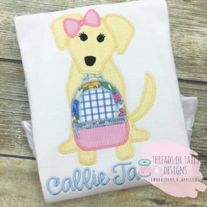 May include: A yellow dog with a pink bow and a blue and pink checkered backpack. The dog is wearing a yellow shirt with the name "Callie Ja" embroidered on it. The image is from Threads or Tails Designs, Embroidery & Applique.