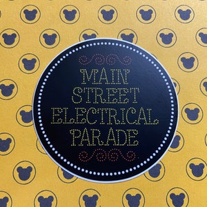 May include: A black and white circular sticker with the text "Main Street Electrical Parade" in yellow lights. The sticker is on a yellow background with a repeating pattern of black bear heads.