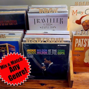 May include: A wooden display case filled with vinyl records, categorized by genre with wooden dividers. Album covers feature artists like Tyler Childers, Chris Stapleton, and Jackie Wilson. A red starburst sign reads "Mix & Match Any Genre!"