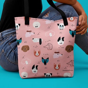 May include: A pink tote bag with a repeating pattern of colorful dog and cat faces. The bag has black straps and the text "DohStyleStudio" is printed on the bottom right corner.