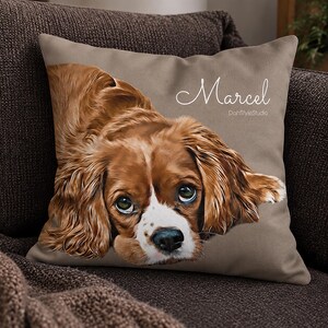 May include: A square throw pillow in a solid taupe color featuring a detailed illustration of a brown and white spaniel dog. The name Marcel is printed in white cursive script above the dog, with the text DohStyleStudio printed below it.