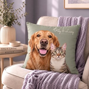 May include: A square sage green throw pillow featuring a printed portrait of a golden retriever and a tabby cat. The text "Rey & Lucy" is printed in white cursive script in the upper right corner of the pillow cover, which is placed on a chair.