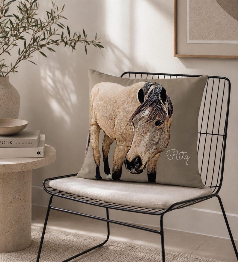 May include: A square throw pillow in a muted taupe color featuring a detailed illustration of a light tan horse with a dark mane and tail. The name Ritz is written in a white cursive script on the right side of the pillow cover.