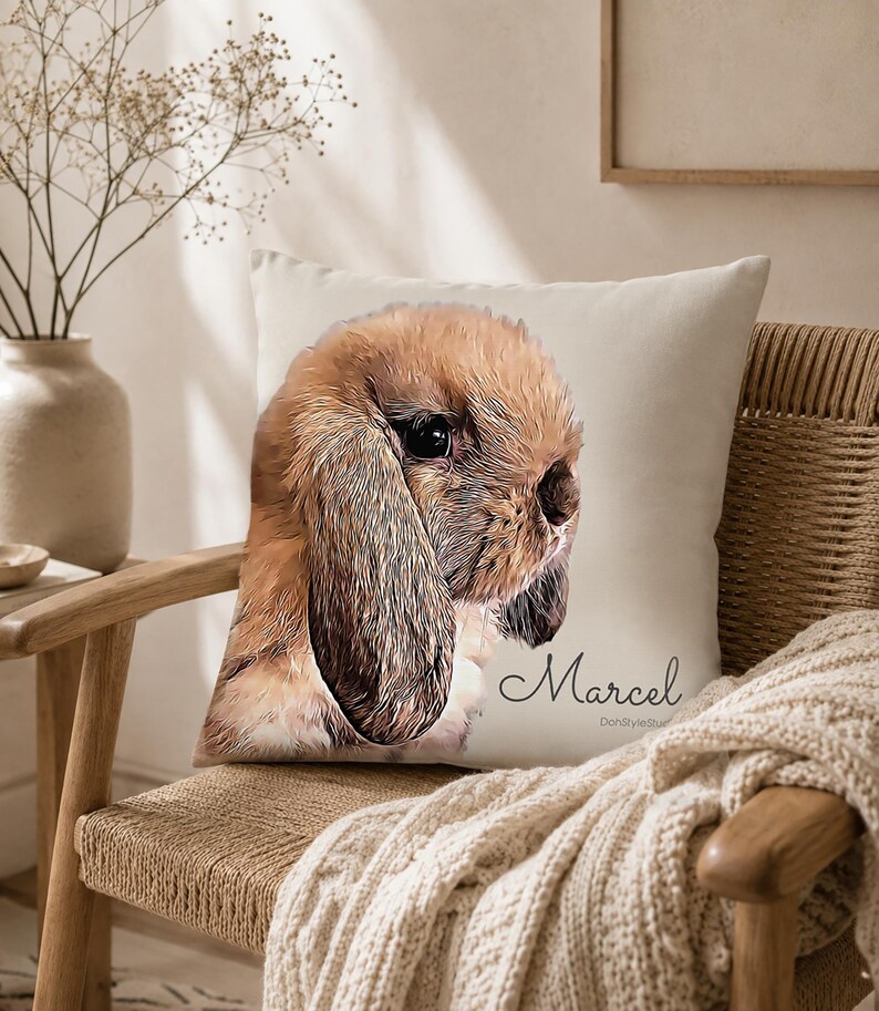 May include: A square throw pillow featuring a printed illustration of a brown lop-eared rabbit. The rabbit has long, soft ears and dark eyes. The name Marcel is printed in a cursive script font below the rabbit illustration on the off-white fabric.