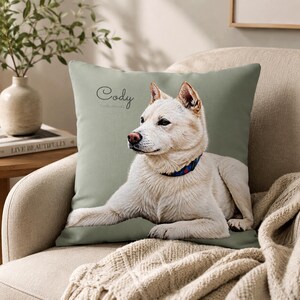 May include: A square throw pillow with a sage green background featuring a realistic illustration of a white dog lying down. The dog wears a blue collar with red and white accents. The name Cody is printed in a black script font above the dog.