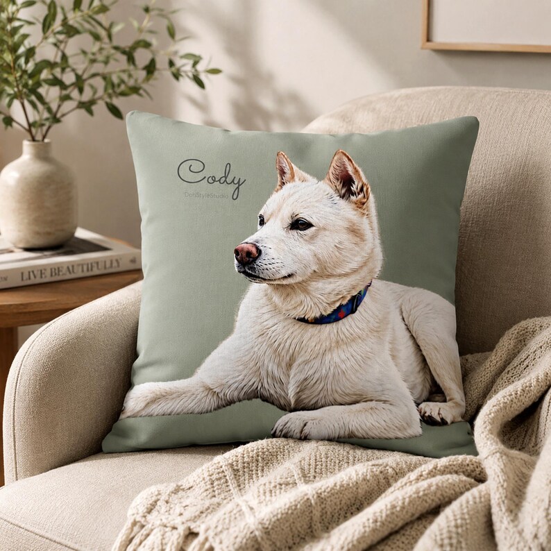 May include: A square throw pillow with a sage green background featuring a realistic illustration of a white dog lying down. The dog wears a blue collar with red and white accents. The name Cody is printed in a black script font above the dog.