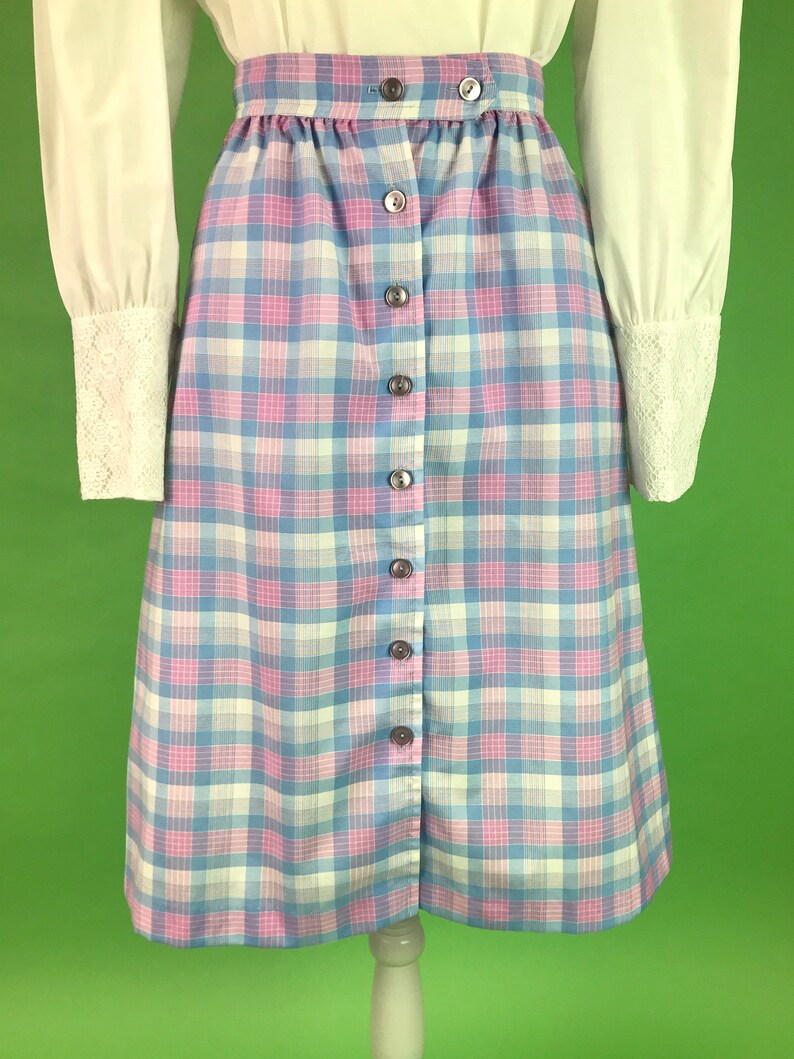 Op de afbeelding: Een blauwe en roze geruite rok met een knoopsluiting aan de voorkant. De rok is knielengte en heeft een geplooide taille.