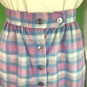 Op de afbeelding: Een blauwe, roze en witte geruite rok met knoopsluiting. De rok heeft een hoge taille en is gemaakt van een lichtgewicht stof.