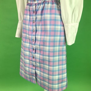 Op de afbeelding: Een blauwe en roze geruite rok met een knoopsluiting aan de voorkant. De rok is knielengte en heeft een hoge taille.