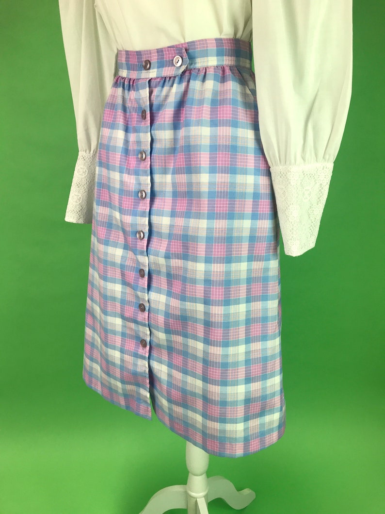Op de afbeelding: Een blauwe en roze geruite rok met een knoopsluiting aan de voorkant. De rok is knielengte en heeft een hoge taille.
