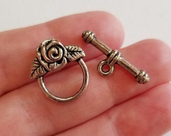 May include: Silver-toned metal toggle clasp with a rose design. The clasp has a round ring and a bar with a loop on one end.