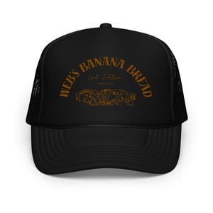 May include: Black trucker hat with a curved brim and mesh back. The hat features the text "WEB'S BANANA BREAD" in a brown, arched font, with "Limited Edition" below. A brown illustration of banana leaves is centered below the text.