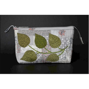 Peut inclure: Une pochette en tissu patchwork gris et blanc avec une fermeture à glissière et un motif de feuilles brodées en vert.