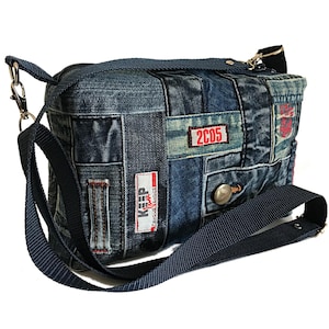 Può includere: Borsa a tracolla in denim con design patchwork. La borsa presenta una tracolla regolabile blu scuro e hardware color argento. Sono visibili toppe con il testo "KEEP" e "2C05". La borsa è larga circa 30 cm.