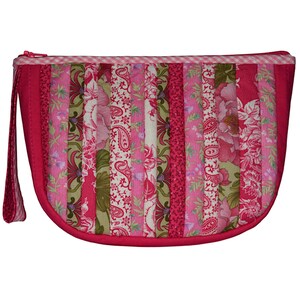 Może przedstawiać: Pikowana kosmetyczka w kształcie półksiężyca z paskiem na nadgarstek. Kosmetyczka posiada pionowe paski z różowych i zielonych tkanin kwiatowych i paisley. Górna krawędź wykończona jest różowo-białą tkaniną w kratkę i różowym zamkiem błyskawicznym.