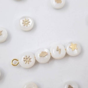 May include: A string of white round beads with gold accents. Each bead features a different weather-themed design, including a sun, a cloud, a lightning bolt, and a star.