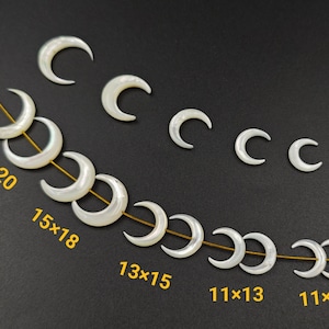 Pode incluir: Um fio de contas de lua crescente de madrepérola branca em vários tamanhos. As contas são enfiadas em um fio dourado. Os tamanhos das contas são etiquetados em polegadas: 18x20, 15x18, 13x15, 11x13 e 11x12.
