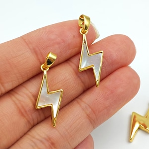 May include: Three gold-tone lightning bolt pendants with white mother-of-pearl inlays. The pendants are on a white background.