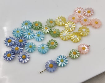 May include: Assortment of colorful flower-shaped beads in shades of blue, green, yellow, and pink. The beads have a pearlescent finish and yellow centers.