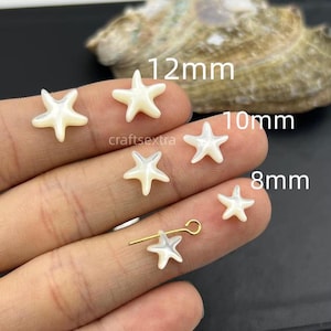 May include: A collection of white, iridescent, star-shaped shell beads in three sizes labelled 12mm, 10mm, and 8mm. One star bead is attached to a gold-toned metal eye pin. The beads have a smooth, polished finish and a five-pointed star shape.