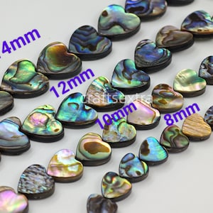 Op de afbeelding: Meerdere strengen hartvormige abalone schelpkralen met iriserende oppervlakken in tinten groen, blauw en paars. De afbeelding bevat paarse tekstlabels die de maten 14mm, 12mm, 10mm en 8mm aangeven, samen met de tekst craftsextra.