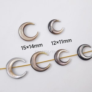 May include: Six crescent moon-shaped beads with a pearlescent finish. Two beads are labeled with dimensions 15x14mm and 12x11mm. Four of the beads are strung on a thin gold-colored wire, while two are loose. The beads feature a smooth, curved surface.