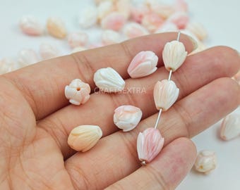 May include: A collection of small, carved shell beads shaped like tulip flower buds in shades of pale pink, cream, and white. Three beads are strung on a thin metal wire, while several others are scattered loosely. The text CRAFTSEXTRA is visible.