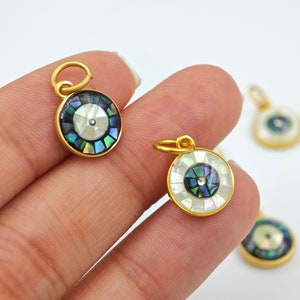 May include: Gold-toned pendant charms with a blue and white eye design. The eye is made of iridescent mother of pearl and is surrounded by a gold-toned frame.