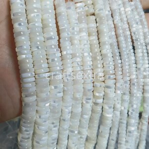 May include: Multiple strands of white mother of pearl beads shaped like small, flat discs. Each bead has a smooth, iridescent surface with a subtle sheen. The beads are strung together on thin, clear filaments, creating long, uniform vertical lines.