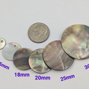 Puede incluir: Surtido de seis discos redondos de nácar iridiscente con un agujero en el centro. Los discos varían en tamaño de 10 mm a 30 mm de diámetro.