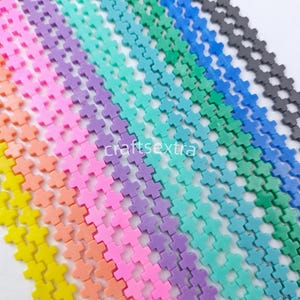 May include: Multiple strands of small, cross-shaped beads arranged in a diagonal rainbow gradient. The colors include yellow, orange, pink, purple, teal, green, blue, and black. The text "craftsextra" is visible in the center of the image.
